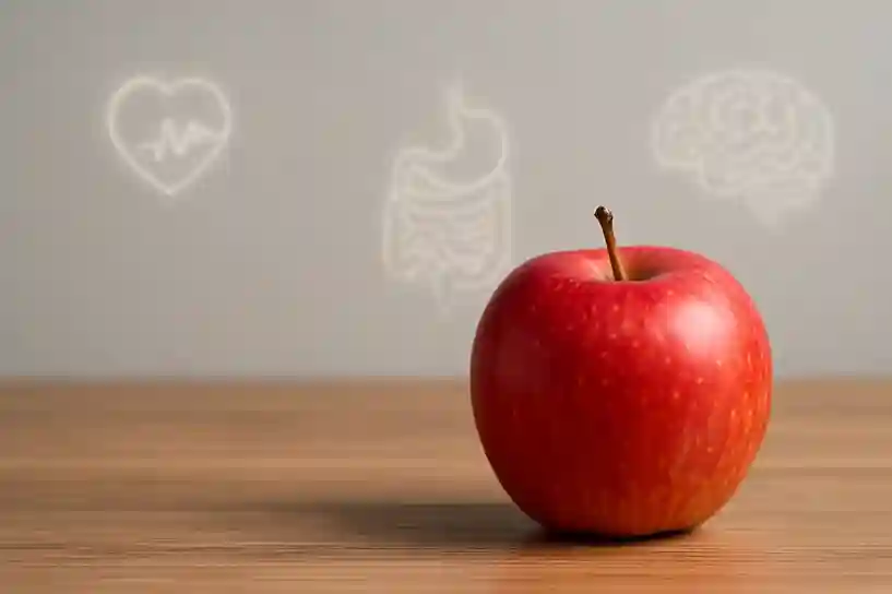 Fresh red apple on a wooden table with glowing icons of a heart, digestive system, and brain in the background, symbolizing apples and health benefits.