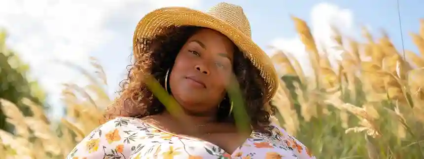 Plus-size woman wearing a floral midi dress and sneakers, smiling confidently in an outdoor setting.