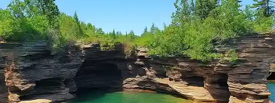 Scenic Sandstone Cliffs of the Apostle Islands Sandstone cliffs and sea caves along the Apostle Islands shoreline with clear turquoise waters under a bright blue sky.